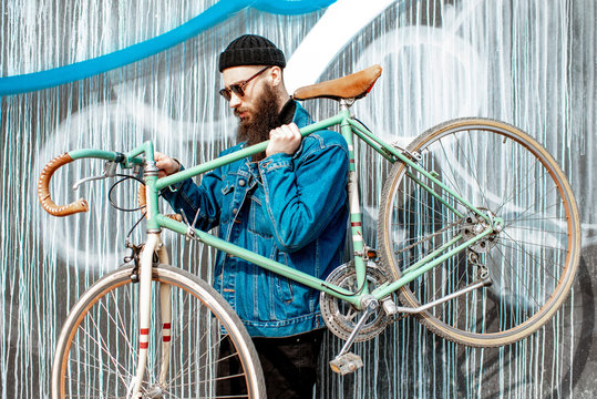 Portrait of a stylish bearded man dressed in jacket and hat with retro bicycle on the colorful wall background