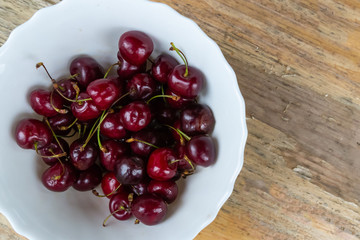 white bowl of red cherry dark berry close-up of many fruits on a wooden background