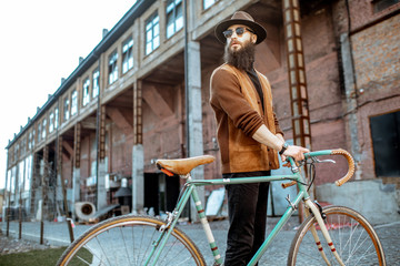 Lifestyle portrait of a bearded hipster dressed stylishly walking with retro bicycle on the...