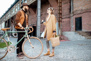 Stylish young man and woman having a conversation standing together with retro bicycle outdoors on the industrial urban background