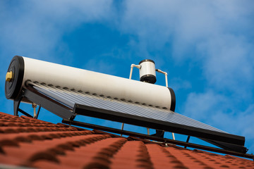 Solar water heater boiler on rooftop, blue sky with white clouds in the background.