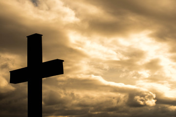 Simple wood catholic cross silhouette, dramatic orange storm clouds in the background, copy space.