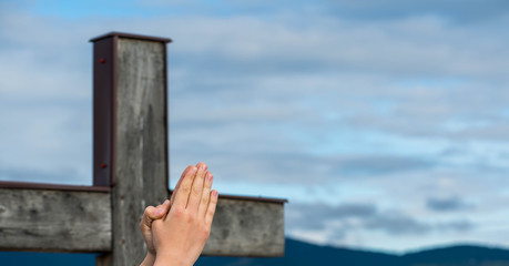 Praying young boys hand in focus, simple wooden catholic cross in the background, copy space.