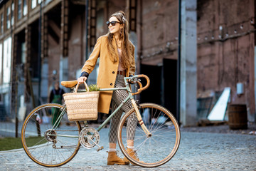 Full body portrait of a beautiful stylish woman dressed in coat standing with retro bicycle...