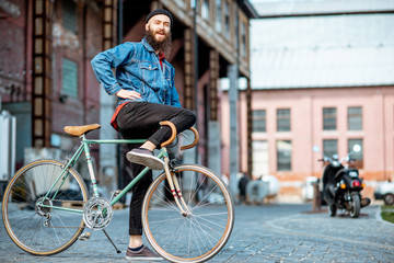Fototapeta premium Portrait of a bearded man as a crazy hipster having fun with retro bicycle outdoors on the industrial urban background