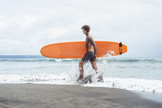 Attractive male surfer in tattoos on the ocean with an orange bright longboard surfboard. Bali Canggu indonesia surfing