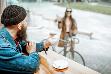 Stylish man meeting his girlfriend with bicycle while sitting with coffee near the window at the...