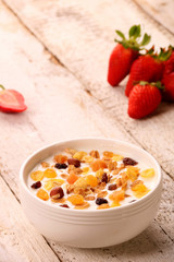 Bowl of yogurt with strawberries and granola muesli, over a white wood background.