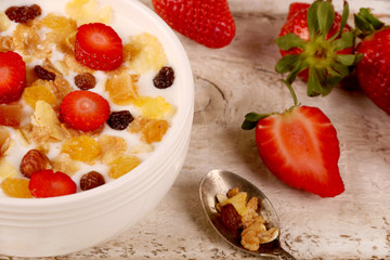 Bowl of yogurt with strawberries and granola muesli, over a white wood background.