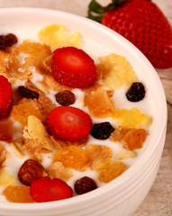 Bowl of yogurt with strawberries and granola muesli, over a white wood background.