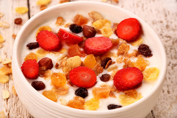 Bowl of yogurt with strawberries and granola muesli, over a white wood background.