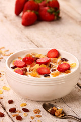 Bowl of yogurt with strawberries and granola muesli, over a white wood background.