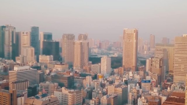 Drone panning above Tokyo city at sunset with orange hazy skies and a birds eye view of commercial skyscrapers