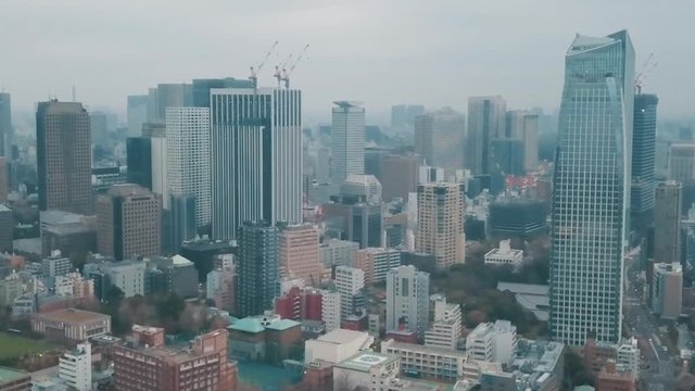 Aerial drone panning up towards the Tokyo city skyline in Japan on an overcast day with hazy smog filled skies and grey storm clouds above busy roads and skyscrapers