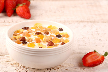 Bowl of yogurt with strawberries and granola muesli, over a white wood background.