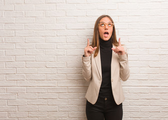 Young pretty business entrepreneur woman surprised pointing up to show something