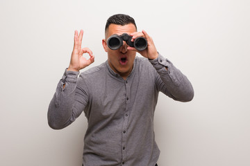 Fototapeta premium Latin man cheerful and confident doing ok gesture. He is holding a binoculars.
