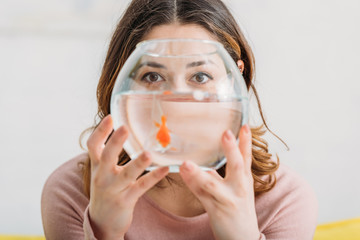selective focus of woman holding aquarium with bright gold fish and looking at camera