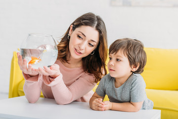 pretty woman holding fish bowl with bright gold fish near adorable son