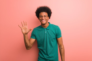 Young african american man over a pink wall showing number five