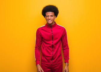 Young sport black man over an orange wall winking, funny, friendly and carefree gesture