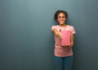 Young black woman reaching out to greet someone. She is holding a popcorns bucket.