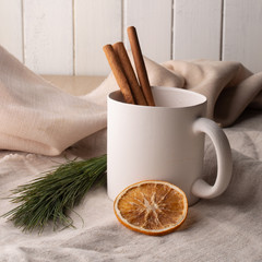 Handmade white ceramic cup, pottery, on the background of linen fabric, with dried oranges and real cinnamon sticks