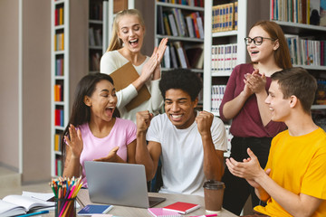Group of young euphoric students enjoying test results in library