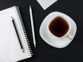 Office concept. Black and white pencils, blank notebook and white cup with coffee on black and white paper background. Top view. Copy space
