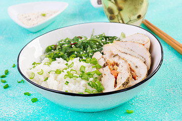 Healthy salad in a white bowl, chopsticks. Chicken rolls, rice, chuka and green onion. Blue background. Asian cuisine.