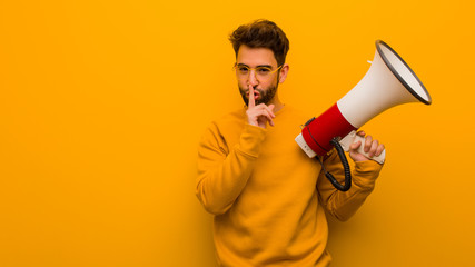 Fototapeta premium Young man holding a megaphone keeping a secret or asking for silence