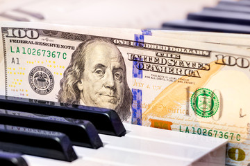 US Dollars lie on the piano keys. Payment for the concert, profit from performing musical works_