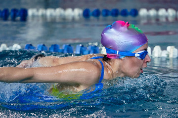 Female athlete swims with a butterfly style. Splashes of water scatter in different directions.
