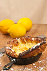 Top, front view, close distance of a freshly prepared, homemade, german pancake on a cast iron fry pan with three lemons on a wood cutting board