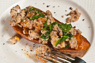 Top view, close distance of a baked sweet potato skin filled with grilled italian sausage  and sautéed spinach, on a round, white plate with an artisan fork