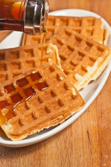 Top view, close distance of four, freshly baked, homemade, waffles with maple syrup pouring over the top on a oval, white plate