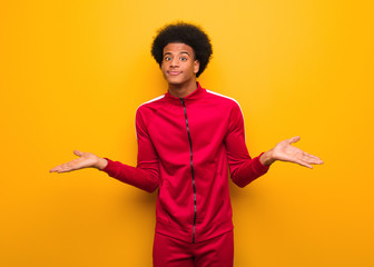 Young sport black man over an orange wall doubting and shrugging shoulders
