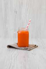 Carrot smoothie in a glass jar on a white wooden background, side view.