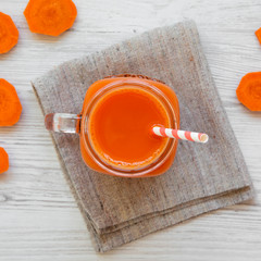 Carrot smoothie in a glass jar on a white wooden background, overhead view. Flat lay, top view, from above.