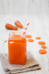 Carrot smoothie in a glass jar on white wooden surface, side view. Close-up.