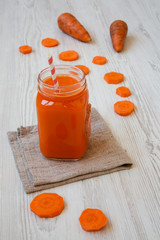 Carrot smoothie in a glass jar on a white wooden surface, side view. Close-up.