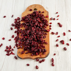 Dry organic cranberries on rustic wooden board over white wooden background, low angle view. Close-up.