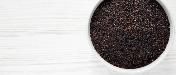 Gluten-free raw organic black quinoa in a bowl over white wooden background, top view. From above, overhead, flat lay. Copy space.