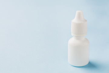 White bottle on a blue background. Round white plastic bottle for medical or cosmetic liquid, eye drops, oil. Side view.