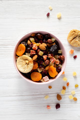 Dried fruits and nuts in a pink bowl over white wooden table. Top view, from above, flat lay. Close-up.