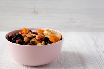 Dried fruits and nuts in a pink bowl over white wooden background, side view. Copy space.