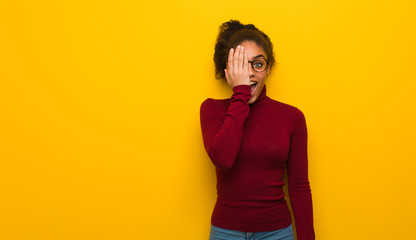 Obraz premium Young black african american girl with blue eyes shouting happy and covering face with hand