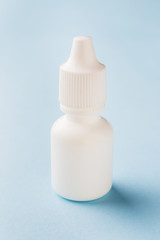 White bottle on a blue background. Round white plastic bottle for medical or cosmetic liquid, eye drops, oil. Side view.