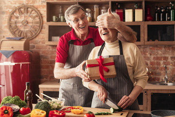 Senior woman receiving gift from her loving husband in kitchen