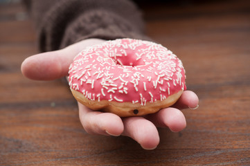 closeup of pink doughnut in hand on wooden table background